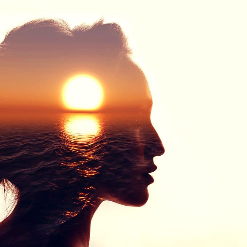Silhouette of woman's head with sunset inside on off-white background.