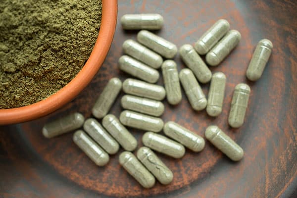Terra cotta bowl and clear capsules containing powdered kratom.