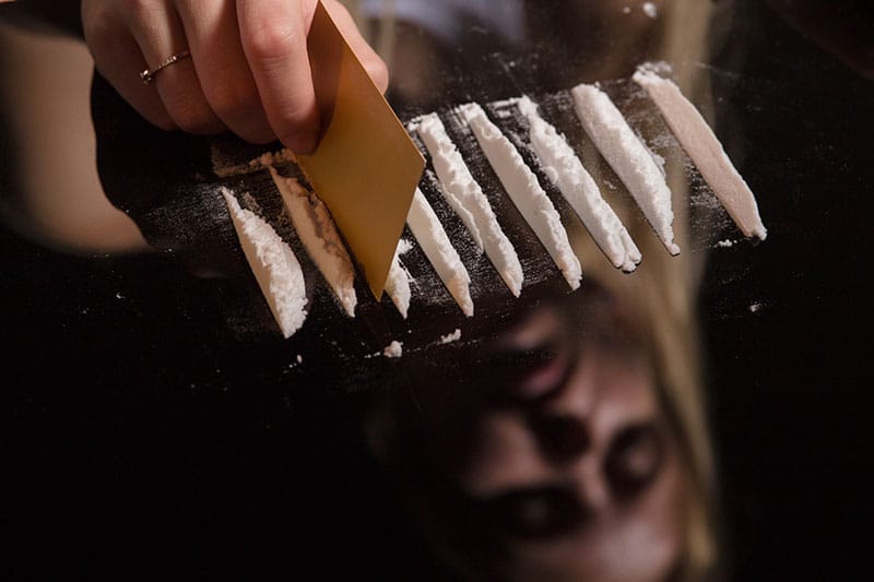 A woman using a credit card to cut lines of cocaine on a mirror.