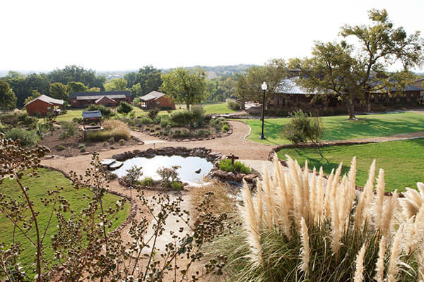 Wide aerial shot of reflecting pond, walking paths, and cabins at Enterhealth Ranch.