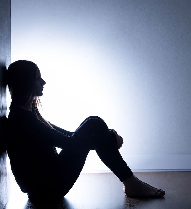 Depressed looking woman sitting on the floor in a dimly lit room.