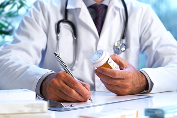 Doctor in white coat holding a bottle of prescription medication and writing on a clipboard.