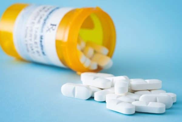 White prescription pills spilling out onto a light blue table.
