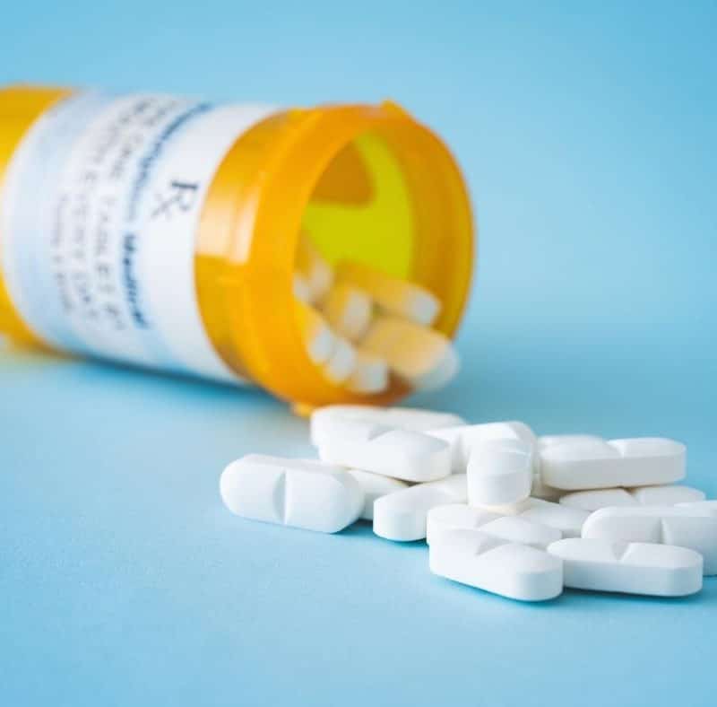 White prescription pills spilling out onto a light blue table.
