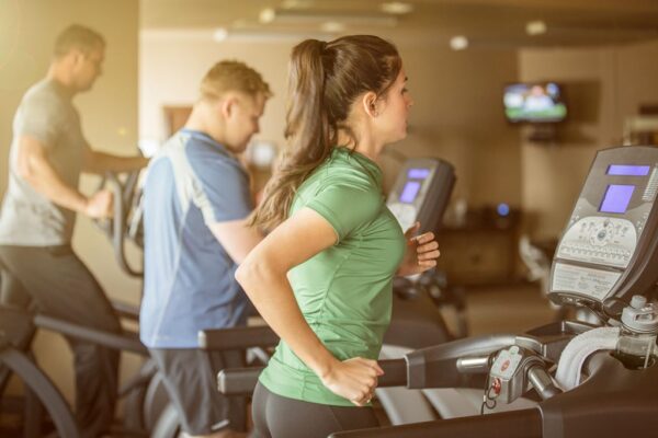 Woman and two men working out in a fitness room on treadmills and elliptical.