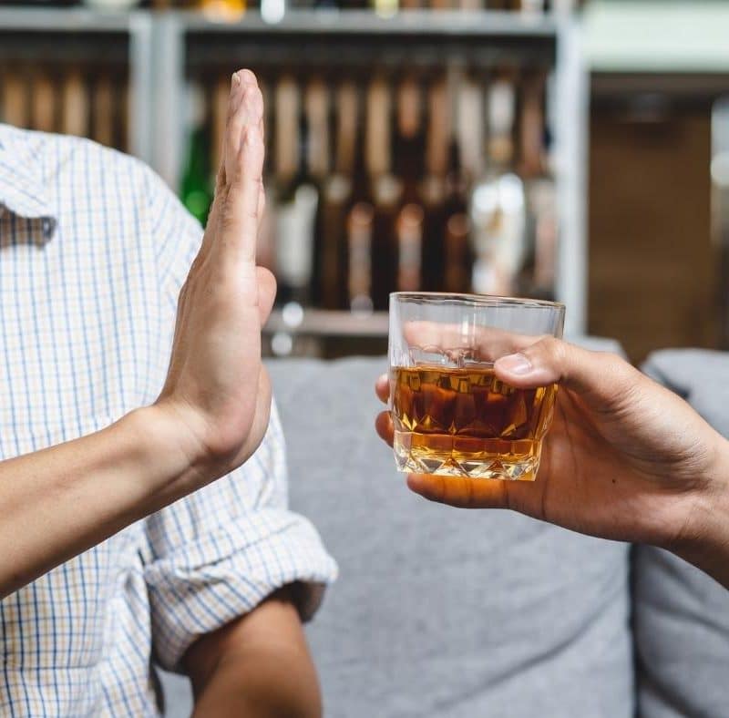 A man who knows how to stop drinking holds up his hand to decline a drink being offered to him.