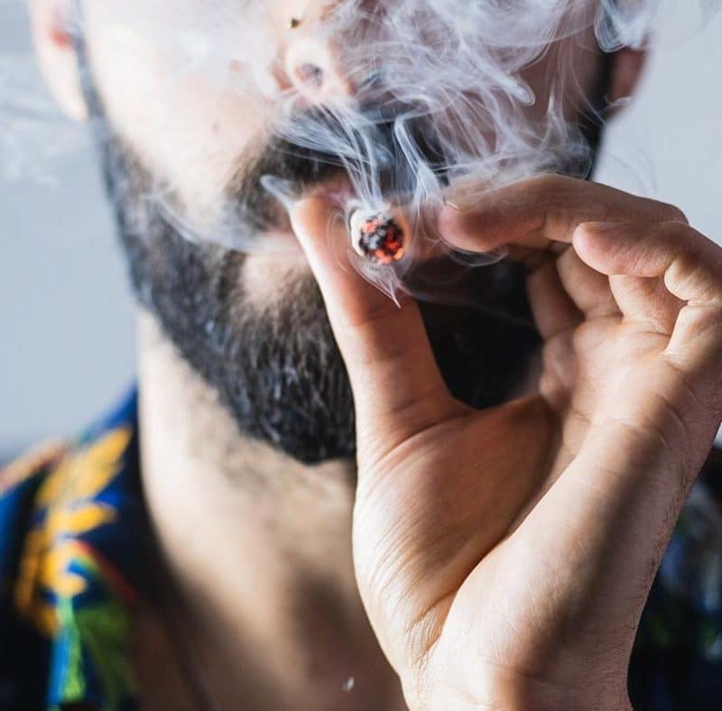 Man with a beard smoking weed in a joint.