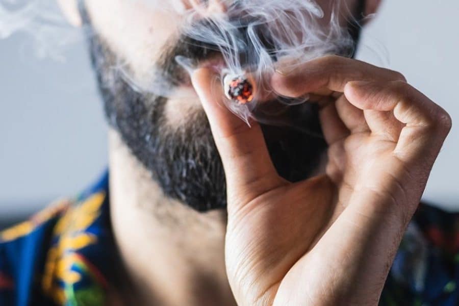 Man with a beard smoking weed in a joint.
