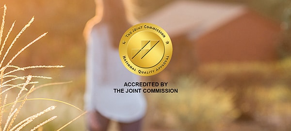Joint Commission accreditation badge with out-of-focus woman walking down an outdoor path in background.