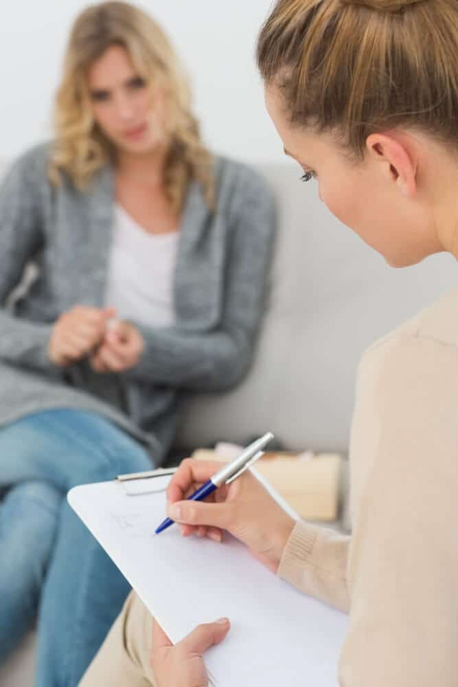 Female therapist writing on clipboard while talking to patient.
