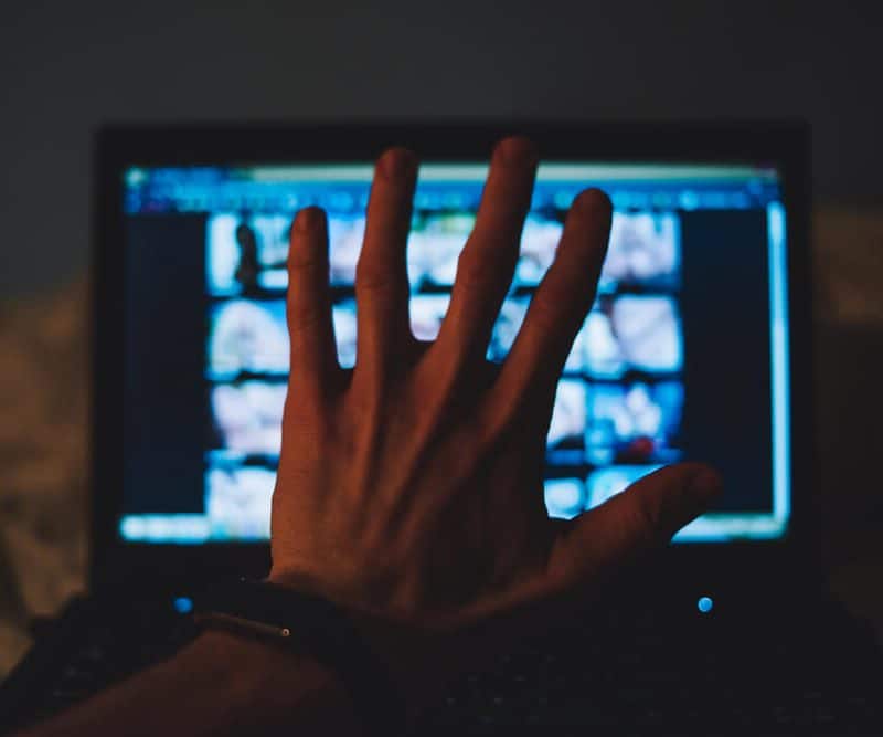 POV of a person holding up their hand blocking a laptop displaying a porn site.
