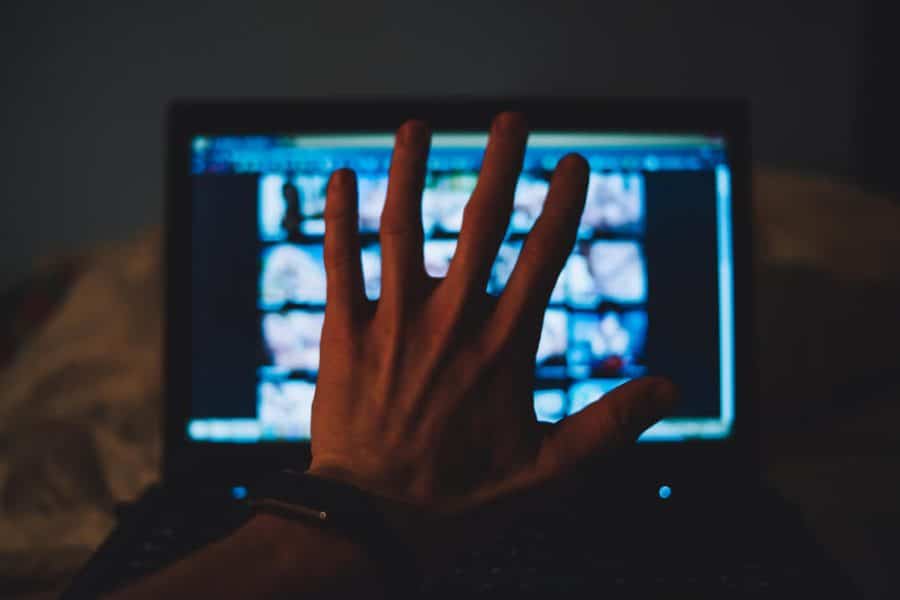 POV of a person holding up their hand blocking a laptop displaying a porn site.