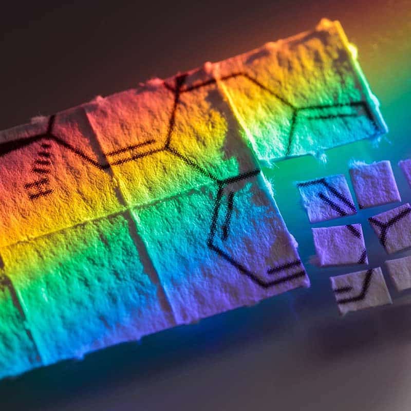 LSD (acid) blotter paper cut up into tiny pieces for microdosing, with rainbow shining on it.