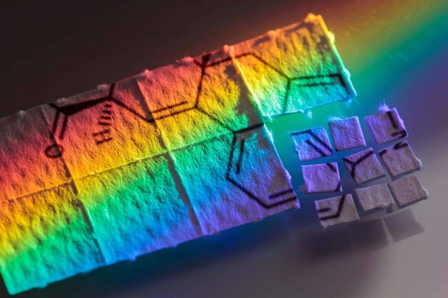 LSD (acid) blotter paper cut up into tiny pieces for microdosing, with rainbow shining on it.