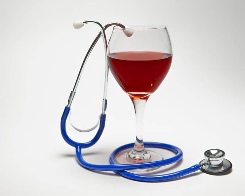 Glass of red wine intertwined with a doctor's stethoscope on a white background.