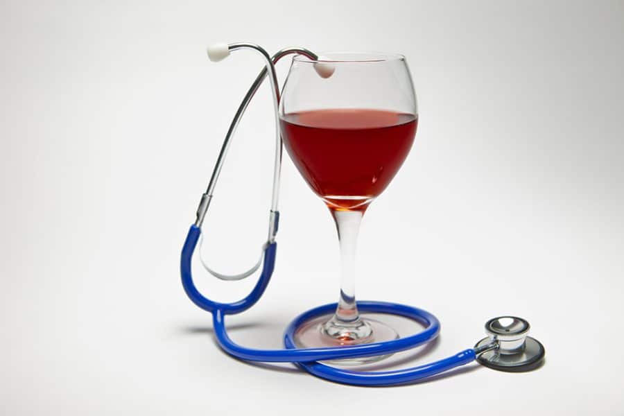 Glass of red wine intertwined with a doctor's stethoscope on a white background.