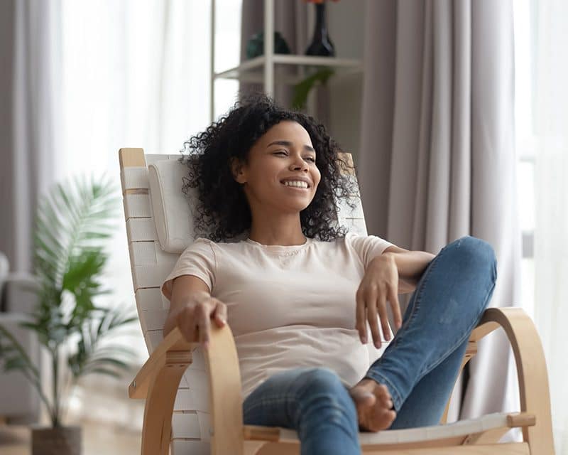 Woman taking time for self-care, relaxing in comfortable chair smiling and looking out the window.