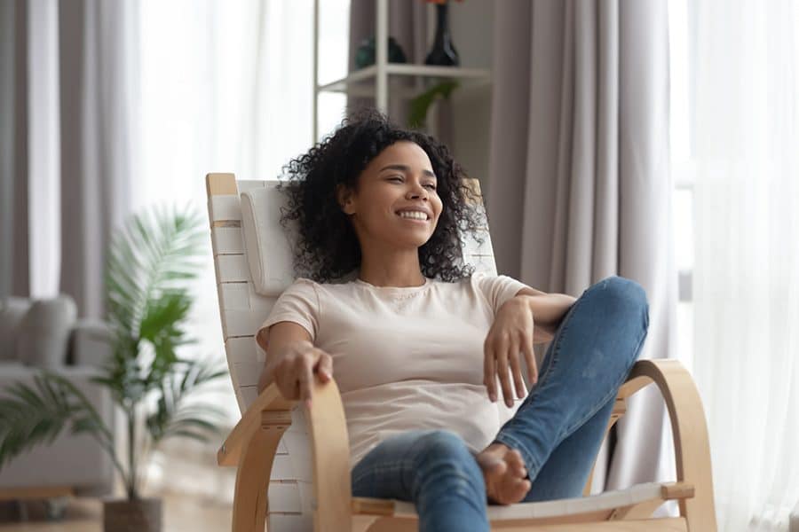 Woman taking time for self-care, relaxing in comfortable chair smiling and looking out the window.