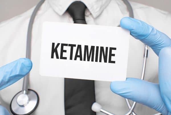 Doctor wearing blue latex gloves holding up and pointing to a card that says "Ketamine".