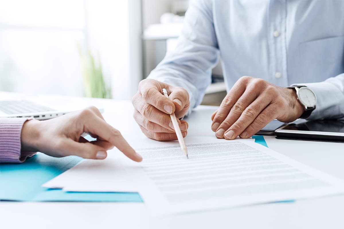 Two people going over paperwork, close up of their hands and papers on white table.